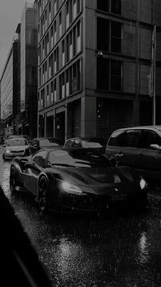 a black and white photo of cars driving down the street in the rain on a rainy day