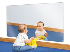 a baby sitting on the floor in front of a mirror looking at it's reflection