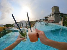 two people holding drinks in front of an outdoor swimming pool