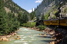 a yellow train traveling down tracks next to a forest filled mountain side covered in trees