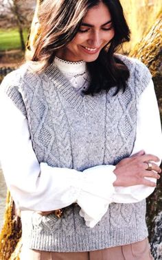 a woman standing in front of a tree with her arms crossed and wearing a sweater