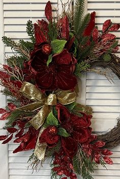 a wreath with red flowers and greenery hanging on the front door, next to shutters