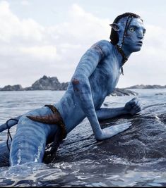 a man with blue paint on his body laying in the water next to a rock