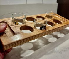 a person holding a wooden tray with three glasses on it and spoon in the middle