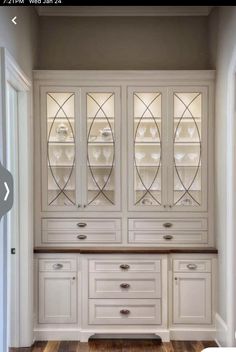 a white china cabinet with glass doors and drawers in the middle of a wooden floor