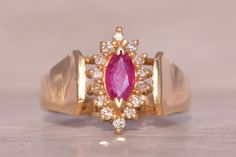 The Stockport: Vintage 1980's Ruby Navette Ring with Natural Diamonds. This captivating ring features a stunning 0.31 carat marquise brilliant-cut natural ruby, boasting a medium purplish-red color that's strong in saturation, creating a striking centerpiece. Surrounding the ruby is a navette-shaped halo set with round brilliant-cut natural diamonds, totaling 0.14 carats in weight, adding sparkle and brilliance to the design. The ring is completed with a widened yellow gold shank, adding to its elegance and charm. Meticulously crafted in 14 karat yellow gold, this ring exudes sophistication and timeless beauty. Currently sized at 6, it offers the option for adjustment to any finger size for an additional fee upon request. Love this piece, but don't have the money to spend right now?  We of Classic Marquise Ruby Ring With Vvs Clarity, Elegant Marquise Ruby Ring With Vvs Clarity, Vintage Marquise Ruby Rings, Vintage Ruby Ring In Marquise Cut, Navette Ring, Halo Setting, Natural Ruby, Rings Statement, Round Brilliant