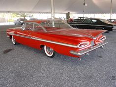 an old red car parked in a parking lot next to other classic cars on display