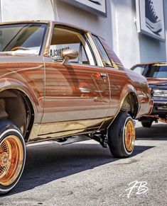 an old car parked in front of a building with gold rims and tires on it