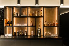 a bar with lots of bottles and glasses lined up on the wall behind it is illuminated by lights