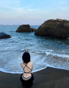 a woman sitting on top of a beach next to the ocean with rocks in the background