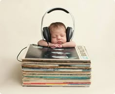 a baby sleeping on top of a stack of records with headphones around his neck