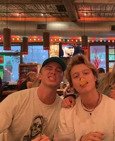 two young men sitting at a table with drinks in front of them and food on their mouths