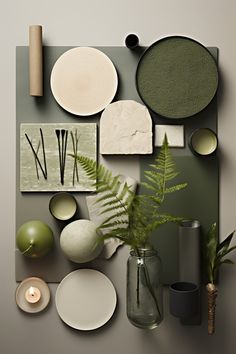 an arrangement of plates, vases and plants on a table with grey walls in the background