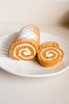 two cinnamon rolls on a white plate with a fork next to one that has powdered sugar on it