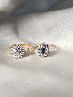 two gold rings with blue and white diamonds on them sitting on top of a white cloth