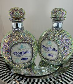 two crystal bottles sitting on top of a glass table next to each other, covered in multicolored jewels