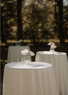 two tables with white tablecloths and flowers in vases on each one side