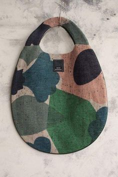 a bib hanging on a wall with an abstract design in green, pink and blue