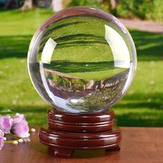 a clear glass ball sitting on top of a wooden table next to pink flowers and grass