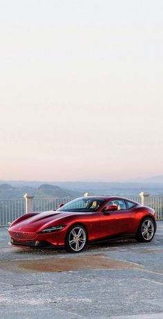 a red sports car parked in a parking lot next to a white fence and mountains