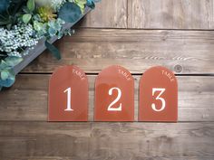 three wooden signs with numbers on them sitting next to a bouquet of flowers and greenery