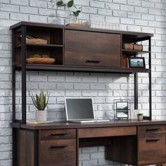 a computer desk with a laptop on top of it next to a white brick wall