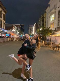 two young women posing for a photo in the middle of an empty street at night