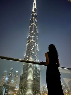 a woman standing on top of a tall building looking at the city lights in the distance