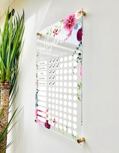 a white wall with a flowered calendar hanging on it's side next to a potted plant