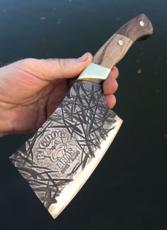 a person holding a knife in their hand near the water with an intricate design on it