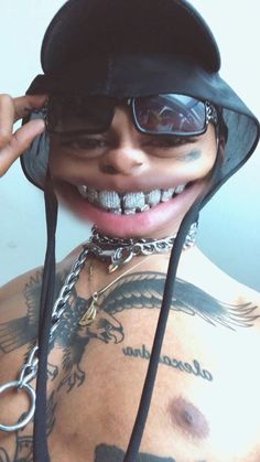 a man with tattoos wearing a black hat and chain around his neck is smiling at the camera