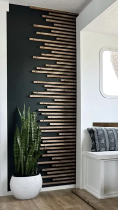 a plant in a white vase next to a black wall with wooden slats on it