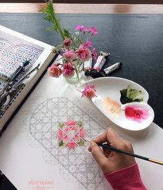 someone is doing something on the table with flowers and paintbrushes in front of them