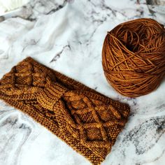 a ball of yarn next to a brown knitted headband on a marble surface