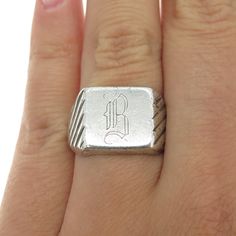 a person's hand with a ring that has the letter b on it and is wearing a silver band