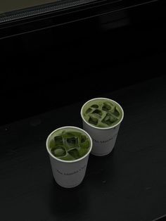 two cups filled with green liquid sitting on top of a black counter next to each other