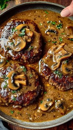 three hamburger patties covered in mushroom gravy on top of a wooden table