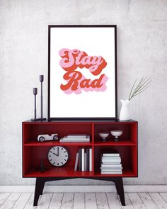 a red bookcase with a clock and vase on it in front of a white wall