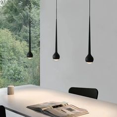 three black lamps hanging from the ceiling above a table with a newspaper on it and two chairs