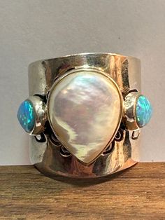 "This is a beautiful, vintage multi stone and sterling silver stamped ring that features a pearl and blue fire opals. The ring is a size 7 and could easily be resized by a jeweler if needed smaller or larger.  The ring face is about 3/4\". The large teardrop pearl measures about 5/8\" in length and has a teardrop-cut blue fire opal on each side of it. Each opal measures about 3/8\" in length and are fiery blue with pinks, greens and purple. So gorgeous. The sterling silver band is stamped with flowers and other symbols. The ring weighs about 8.9 grams and is stamped 925 CFJ Thai. So stunning and a statement piece! See pictures for details. More gorgeous jewelry here, and some on BIG clearance in my shop:  www.etsy.com/shop/BargainBitz Please Note: The display model is not human size and is Stamped Ring, Beautiful Rings Vintage, The Ring Face, Fire Opals, Blue Fire Opal, Stamped Rings, Hippy Gifts, Mother Birthday Gifts, Blue Fire