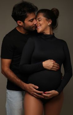 a pregnant couple cuddling and smiling at the camera