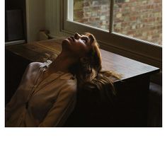 a woman laying on top of a wooden table next to a brick wall and window