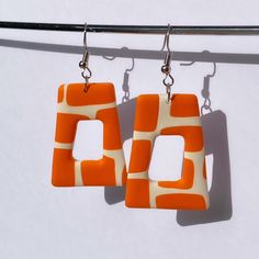 two orange and white square shaped earrings hanging from a hook