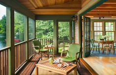 a porch with green chairs and tables on it, overlooking the water's edge