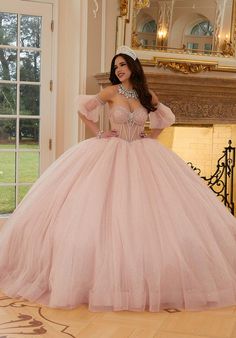 a woman in a pink gown standing next to a fireplace with her hands on her hips