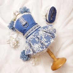 a blue dress and hat laying on top of a white bed next to flowers with a wooden dummy in the foreground