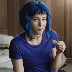 a woman with blue hair is sitting on the floor and brushing her teeth while holding a toothbrush