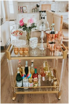 a bar cart filled with bottles and glasses on top of a wooden floor next to a dining room table