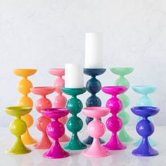 many different colored candles sitting on top of each other in front of a white wall