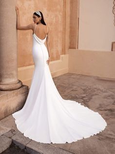 a woman in a white wedding dress leaning against a pillar